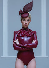A model with a plum fascinator, wearing a plum latex blouse with XL pussy bow and matching high waisted knickers