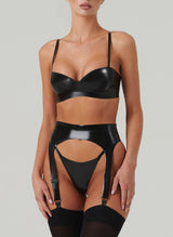 A model wearing a black latex rubber lingerie set, including bra, suspender belt and g-string. Black stockings also worn.
