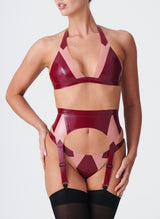 A plum latex lingerie set with Semi-Transparent pink inserts. The latex lingerie set includes a bikini-style halter bra, four strap suspender belt and thong. Model wears black nylon stockings.