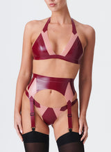 A model wearing a plum latex lingerie set with Semi-Transparent pink inserts. The latex lingerie set includes a bikini-style halter bra, four strap suspender belt and thong. Model also wears black nylon stockings.