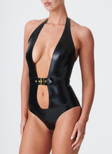 A person wearing a black latex halter body suit with a deep cut-out at the front and a gold metal buckle fastening the built-in belt at the waist. The body suit has a shiny, smooth surface.