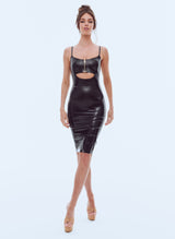 A model wearing a shiny black latex knee-length dress, with a gold metal front zip at the bust and adjustable skinny shoulder straps. On a white background.