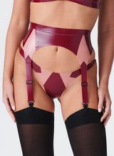 A close up of a model wearing a plum latex suspender belt with pale pink inserts. The belt has four adjustable suspender straps and is worn with a matching thong and black stockings.
