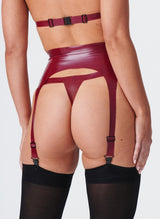 A close up of a model from behind wearing a plum latex suspender belt with pale pink inserts. The belt has four adjustable suspender straps and is worn with a matching thong and black stockings.