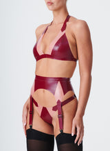 A plum latex lingerie set with Semi-Transparent pink inserts. The latex lingerie set includes a bikini-style halter bra, four strap suspender belt and thong. Model wears black nylon stockings.