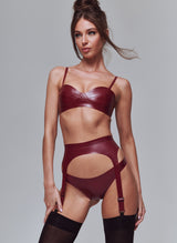 A model wearing a plum latex lingerie set which includes a bra, a four-strap suspender belt, and hipster briefs. The model is also wearing black opaque stockings.
