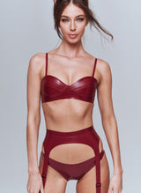 A model wearing a shiny plum latex rubber lingerie set, including bra, suspender belt and hipster briefs.