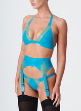 A model wearing an aqua coloured latex lingerie set with Semi-Transparent jade inserts. The latex lingerie set includes a bikini-style halter bra, four strap suspender belt and thong. Model wears black nylon stockings.