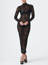 A model wearing a long black lace dress with a high collar and fitted sleeves. The dress features a keyhole at the back neck and a split at the back hem.