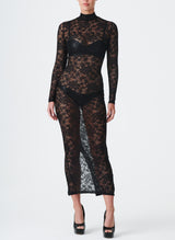 A model wearing a long black lace dress with a high collar and fitted sleeves. The dress features a keyhole at the back neck and a split at the back hem.