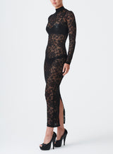 A model wearing a long black lace dress with a high collar and fitted sleeves. The dress features a keyhole at the back neck and a split at the back hem.