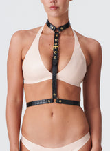A model wearing a peach latex bra and the Natalia Harness, which is made from shiny black leather with gold metal buckles, rings and eyelets.