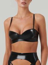 A person wearing a black latex bra with adjustable shoulder straps. The bra is featured in a close-up shot, showcasing its design and fit. Matching suspender belt also in shot, by designer William Wilde.