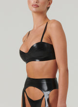 A person wearing a black latex bra with adjustable shoulder straps. The bra is featured in a close-up shot, showcasing its design and fit. Matching suspender belt also in shot, by designer William Wilde.