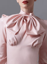 Close up of a baby pink latex pussy bow, worn at the collar of a matching baby pink latex blouse.