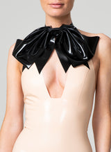A person wearing a black latex pussy bow accessory with a peach latex top.