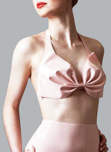 A model wears a pink latex halter neck bra with a large bow at the front cups. Matching high waisted knickers also shown.