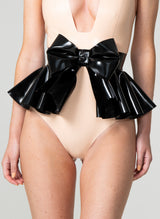 A person wearing a black latex rubber belt with a large bow and flared peplum, fastened with press studs at the back.
