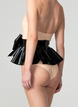 Back view of a person wearing a peach latex bodysuit and a black latex rubber belt with a large bow and flared peplum, fastened with press studs at the back.