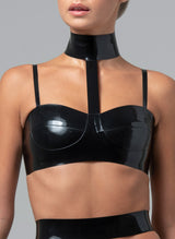 A person wearing a black latex rubber bra with a high neck collar and adjustable shoulder straps.