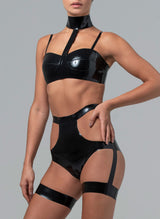 A model wearing a black latex bra and briefs. The bra has skinny shoulder straps and a collar attached, the briefs have cut-outs at the hips and thigh bands attached with straps. By designer William Wilde.