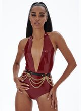 A model wearing a plum latex halter body suit with a deep V-neckline. Worn on top of the bodysuit is a black leather belt with gold chain scallops draped from rings in the belt.