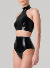 A model on a grey background wears a glossy black latex halter neck cropped top and high-waisted latex knickers.