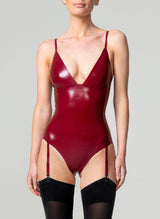 A person wearing a plum latex bodysuit with adjustable shoulder and suspender straps, paired with black opaque stockings.