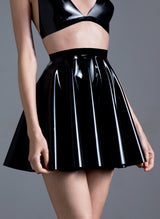 A person wearing a black latex circle skirt with a fitted waistband, paired with a matching latex top. The skirt is flared and falls to mid-thigh.