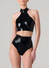 A model on a grey background wears a glossy black latex halter neck cropped top and high-waisted latex knickers.