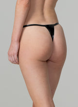 Back view of a person wearing a black latex G-string that features narrow latex straps. The image shows the person from the waist down, focusing on the garment.