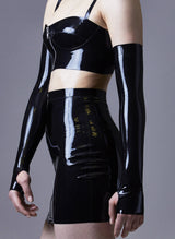 A model wearing long black latex mittens, with matching longline bra and mini skirt, on a grey background.