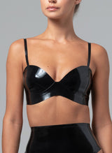 A model wearing a black latex bra with a sweetheart neckline and adjustable shoulder straps. Matching latex suspender belt also in shot, all by designer William Wilde.