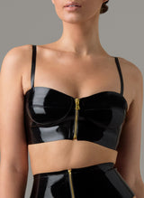 A woman wearing a black glossy latex longline bra with gold front zip and adjustable straps. Matching latex suspender belt also shown.