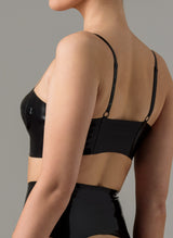 Back of a woman wearing a black glossy latex longline bra with gold front zip and adjustable straps. Matching latex suspender belt also shown.