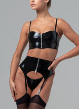 Model wearing a black latex lingerie set on a grey background. The set includes a latex rubber bra and suspender belt with silver metal front zips, and matching latex G-string. Worn here with black stockings.