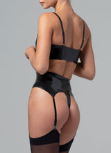 Back view of a model wearing a black latex lingerie set on a grey background. The set includes a latex rubber bra and suspender belt, and matching latex G-string. Worn here with black stockings.