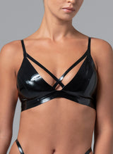 A person wearing a black latex bra with a unique crossover strap detail at the bust. The bra features adjustable shoulder straps and press studs at the back.