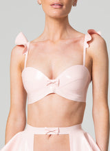 A model wearing a pink latex bra with frilled shoulders and a mini bow at the front. Also matching latex suspender belt, all by designer William Wilde.