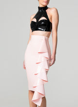 A black latex bra top by William Wilde with a high collar and keyhole cut-outs, worn by a model wearing a pale pink latex skirt against a neutral background.