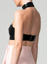 A black latex bra top by William Wilde with a high collar and keyhole cut-outs, worn by a model against a neutral background. Fastening at the back with press studs.