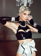 A black latex bra top by William Wilde with a high collar and keyhole cut-outs, worn by a model wearing black latex gloves, grey latex knickers and diamond accessories.