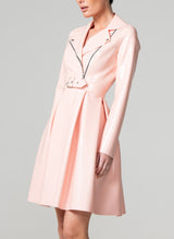 A person wearing a baby pink latex biker Mac with silver metal zip and hardware, long pleated peplum, and a matching belt that is not attached.