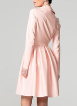 Back shot of a person wearing a baby pink latex biker Mac with metal zip and hardware, long pleated peplum, and a matching belt that is not attached.