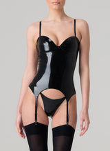 A person wearing a black latex basque with adjustable shoulder straps and suspender straps, featuring a zip fastening at the back, presented against a grey background, and worn with a matching G-string and black stockings.