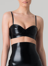 A person wearing a black latex bra with adjustable shoulder straps. The bra is form-fitting and has a glossy appearance. Black latex girdle also in shot, all by designer William Wilde.