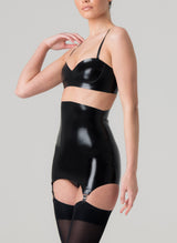 A model wearing a shiny black latex rubber bra and matching girdle with suspender clips at hem. Both by designer William Wilde. Worn here with black nylon stockings.