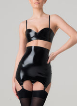 A model wearing a shiny black latex rubber bra and matching girdle with suspender clips at hem. Both by designer William Wilde. Worn here with black nylon stockings.