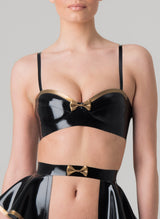 A black latex rubber bra with gold trim, featuring adjustable shoulder straps, a press stud fastening at the back, and a mini bow at the front. Matching latex suspender belt also in shot, all by designer William Wilde.