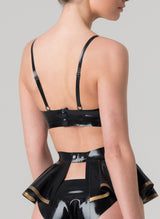 Back shot of a black latex rubber bra with gold trim, featuring adjustable shoulder straps, a press stud fastening at the back, and a mini bow at the front. Matching latex suspender belt and briefs also in shot, all by designer William Wilde.